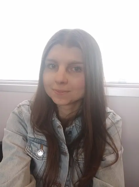 Paulina, młoda kobieta z długimi brązowymi włosami, ubrana w dżinsową kurtkę, uśmiechająca się delikatnie.