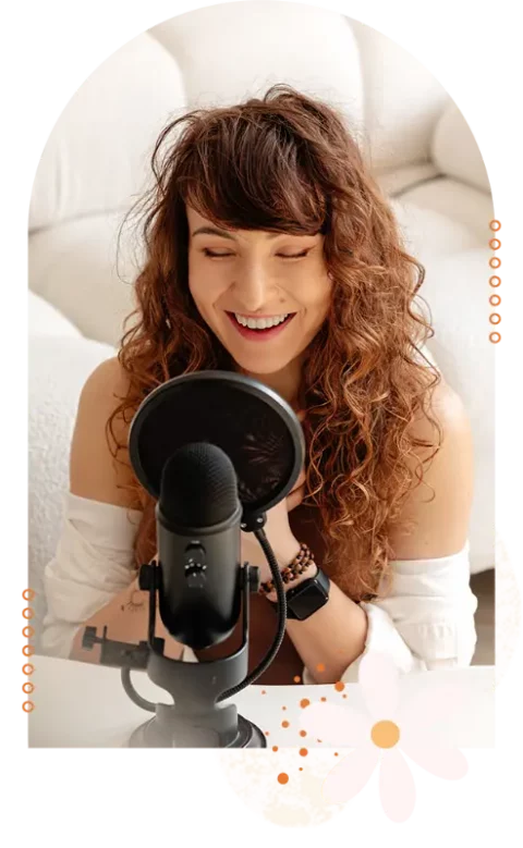 Monika Michalak siedząca na podłodze, uśmiechająca się do mikrofonu stojącego przed nią podczas nagrywania podcastu "Głodna głowa"